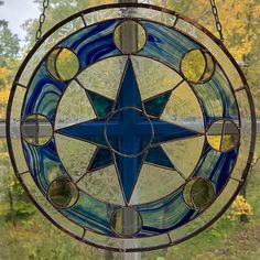 a stained glass sun catcher hanging from a chain in front of a window with trees