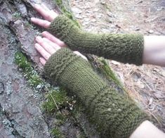 a person wearing green knitted arm warmers standing next to a tree trunk with moss growing on it