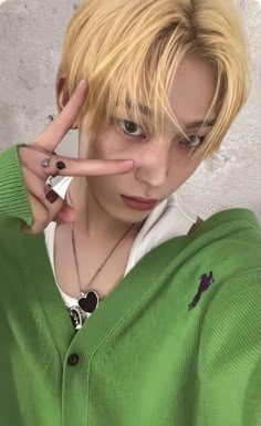 a person with blonde hair making the v sign while wearing a green sweater and white shirt