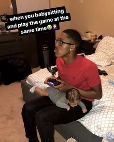 a man sitting on top of a bed holding a baby and texting, when you babysitting and play the game at the same time