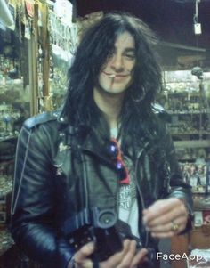 a man with long hair wearing a leather jacket and holding a camera in his hands