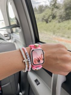 a woman is sitting in her car with two bracelets on her wrist and the watch has pink beads around it