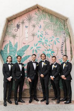 a group of men standing next to each other in front of a wall with plants on it