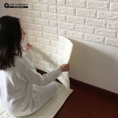 a woman sitting on the floor painting a brick wall with white paint and wood floors