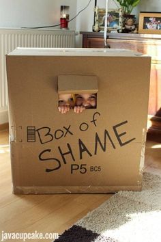 a cardboard box with the words box of shame written on it and someone's face peeking out from inside