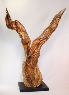 a wooden sculpture on a black base with white backgrounnd and brown woodgrain