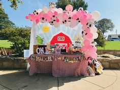 a table with balloons and pictures on it in front of a red barn under a blue sky