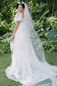 a woman in a wedding dress and veil posing for the camera with greenery behind her