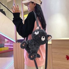 a woman holding a black stuffed animal in her right hand while standing next to an escalator