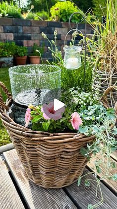 a basket filled with flowers and plants on top of a wooden table next to a candle