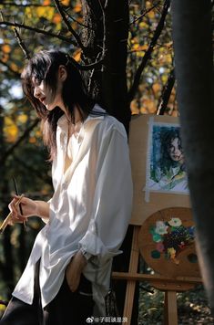 a woman in white shirt painting on easel next to tree