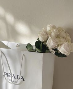 a bouquet of white roses sitting on top of a bag with the word prada in it