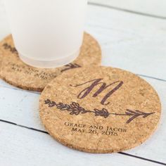 two personalized cork coasters with the names and date printed on them, sitting next to a glass of milk