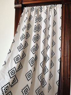 a curtain with black and white designs hanging on a wooden frame in front of a window