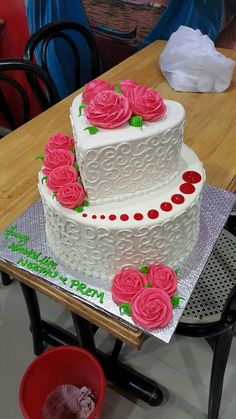 a three tiered cake with pink roses on the top and bottom is sitting on a table