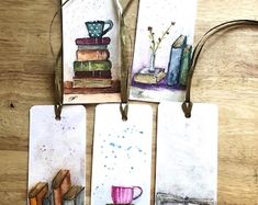 four bookmarks with pictures of books and coffee cups on them, hanging from strings