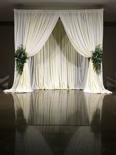 an empty stage with white drapes and greenery