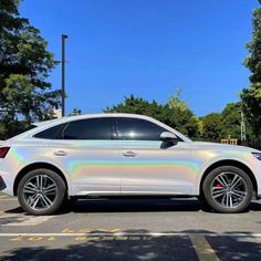 a white car parked in a parking lot with trees and blue sky behind it on a sunny day