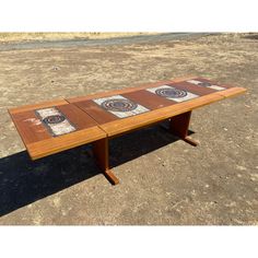 a wooden table sitting in the middle of a dirt field on top of a dry grass field