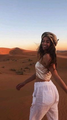 a woman standing in the desert with her arms spread out and smiling at the camera