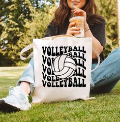 a woman sitting on the grass holding a tote bag with volleyball written on it