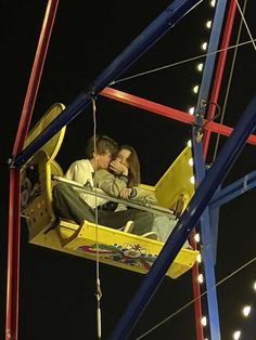 a man and woman sitting in a yellow swing ride at night with lights on the sides