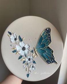 a hand holding a blue and white butterfly on top of a white plate with flowers