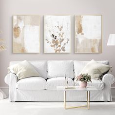 a living room with white couches and paintings on the wall above them, along with a coffee table