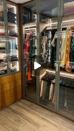 a walk in closet with glass doors and shelves filled with shirts, pants and other items