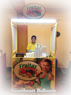 a man standing behind a food cart with fruit on it's sides and smiling at the camera