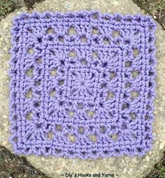 a purple crocheted square sitting on top of a rock