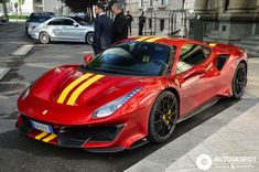 a red sports car with yellow stripes parked on the street next to two men in suits