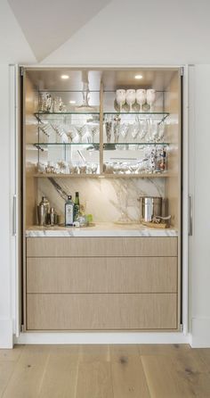 an open cabinet in the middle of a kitchen with wine glasses on it's shelves