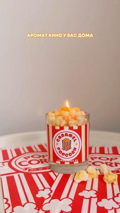 a red and white tray topped with a small cup filled with yellow candies next to a lit candle