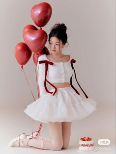 a woman in a white dress holding red balloons