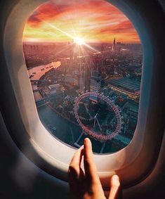 the view out an airplane window shows the london eye in the distance, as the sun sets