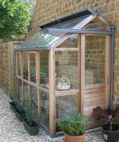 a small wooden greenhouse in the middle of a stone walled garden area with potted plants