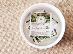 organic raspberry leaf tea packets in a white bowl on a brown carpeted surface