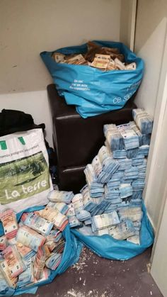 piles of money sitting on top of a floor next to a trash can and bag