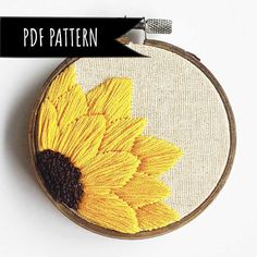 a cross stitch sunflower is shown on a white surface with an embroidered hoop hanging from it's side