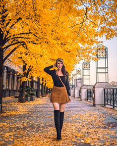 a woman is walking down the street in front of trees with yellow leaves