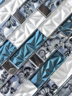 a glass and metal mosaic tile design with blue, white and silver tiles on it