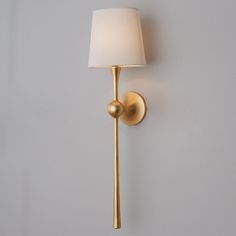 a gold wall light with a white shade on it's side and a gray wall in the background