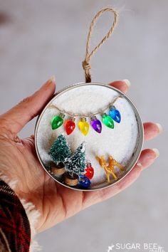 a hand holding a glass ornament with christmas lights and ornaments on it's side