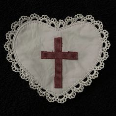 a white heart with a red cross in the center on a black background, decorated with crochet