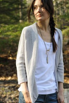 a woman standing in the woods with her hair pulled back and wearing a white shirt