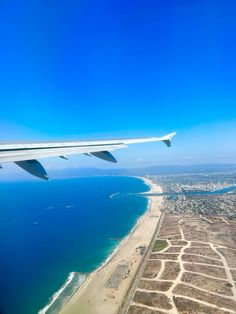 an airplane wing is flying over the ocean and beach area in front of blue skies