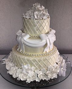 a three tiered wedding cake with white flowers and pearls on the bottom, sitting on a glass platter