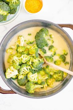 broccoli being cooked in a pot with a wooden spoon and two bowls on the side