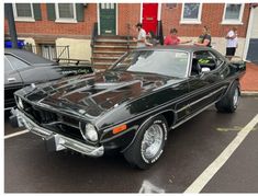 an old black car parked in front of a brick building with people looking at it